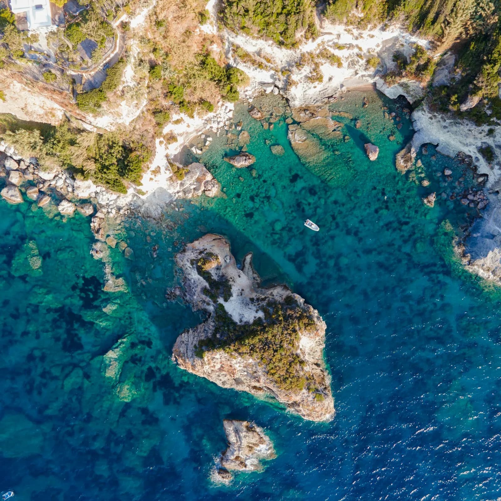 Veduta aerea di una cala rocciosa di Ponza con acqua turchese, scogli affioranti e una piccola barca all'ancora