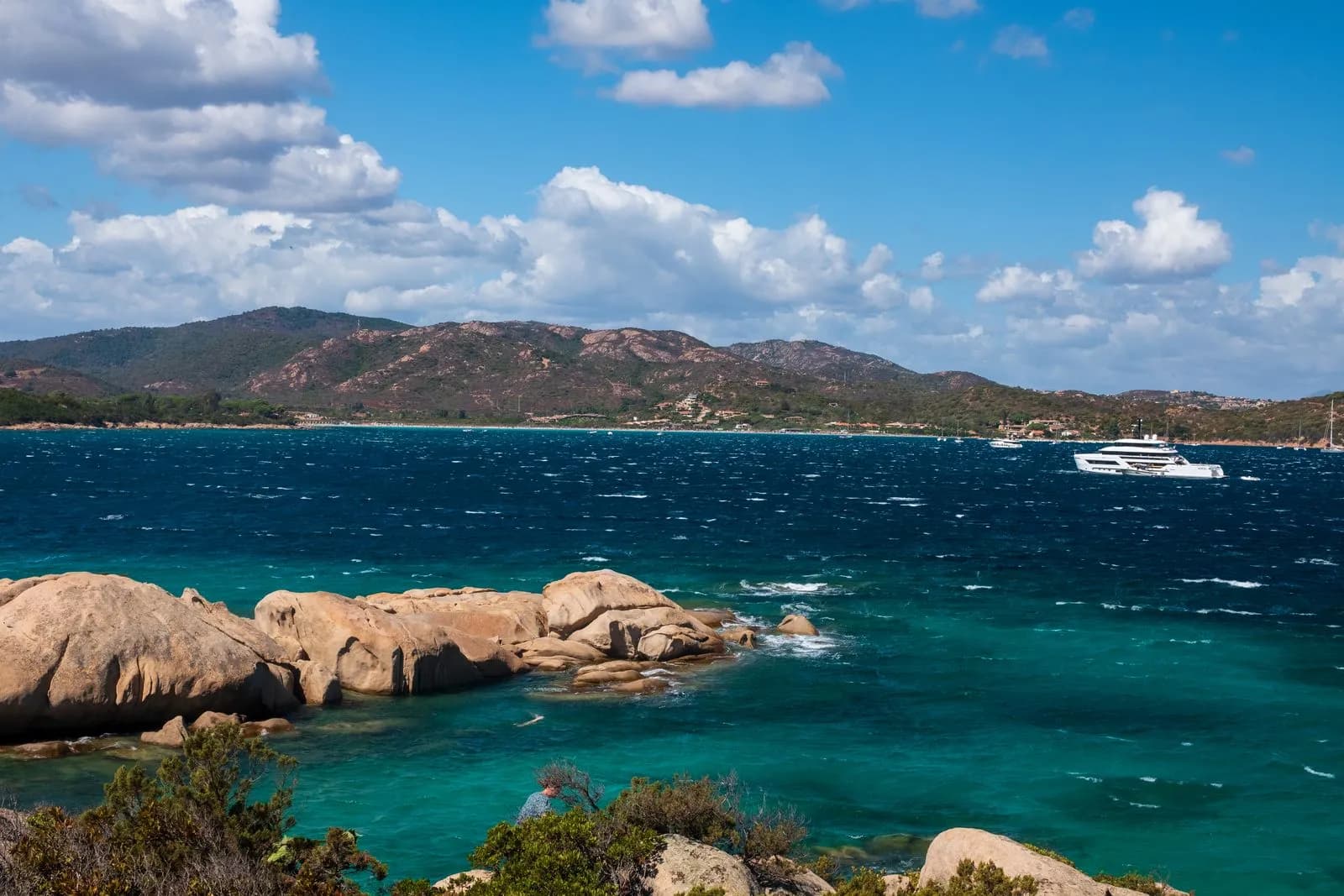 Costa rocciosa della Sardegna con acque turchesi e uno yacht all'ancora