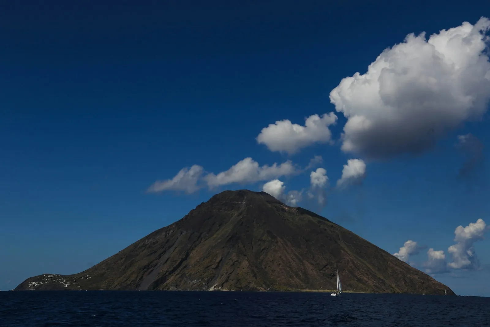 Barca a vela nel mare delle Isole Eolie davanti a un'isola vulcanica