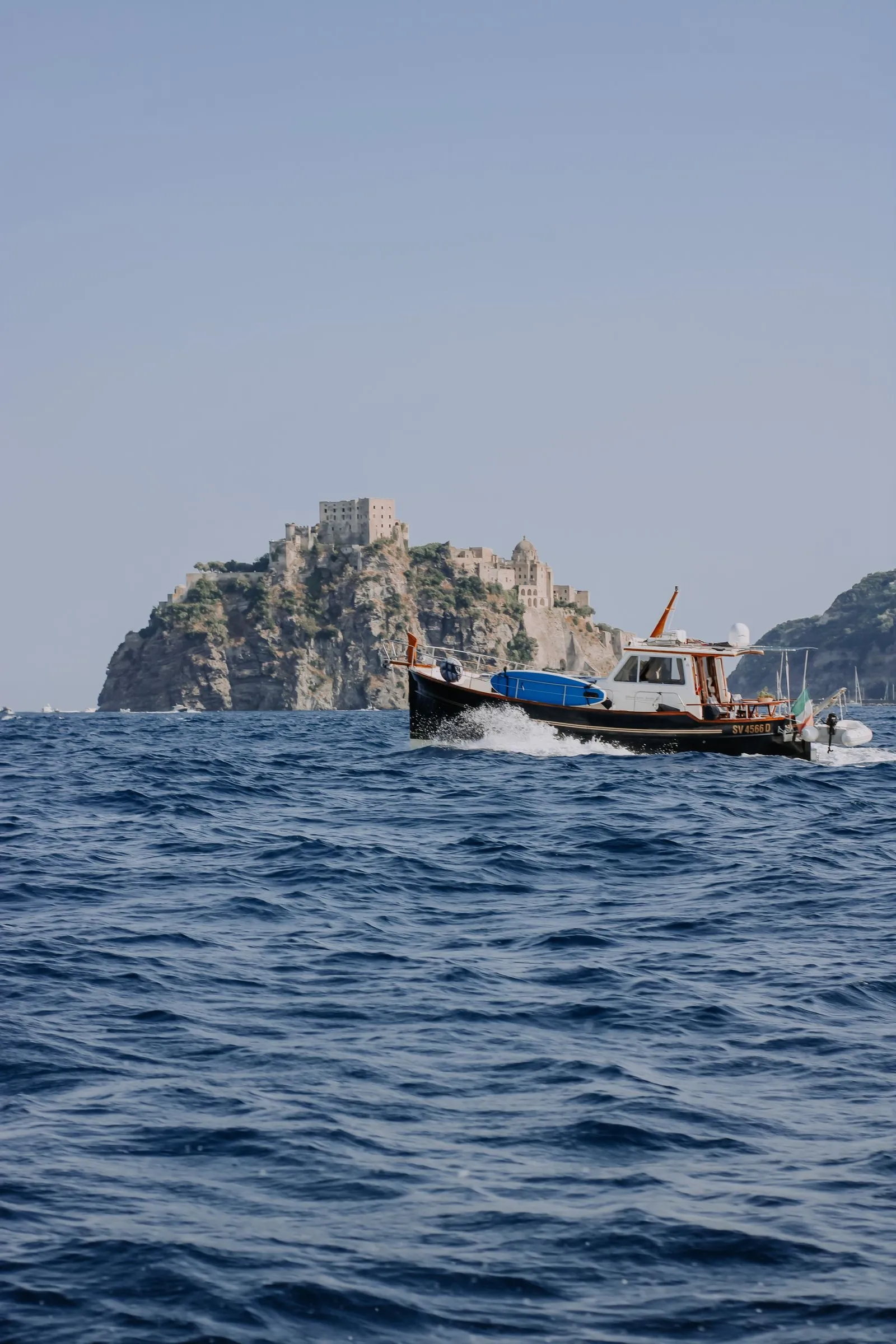 Piccola barca in navigazione davanti al Castello Aragonese di Ischia durante un giro dell'isola