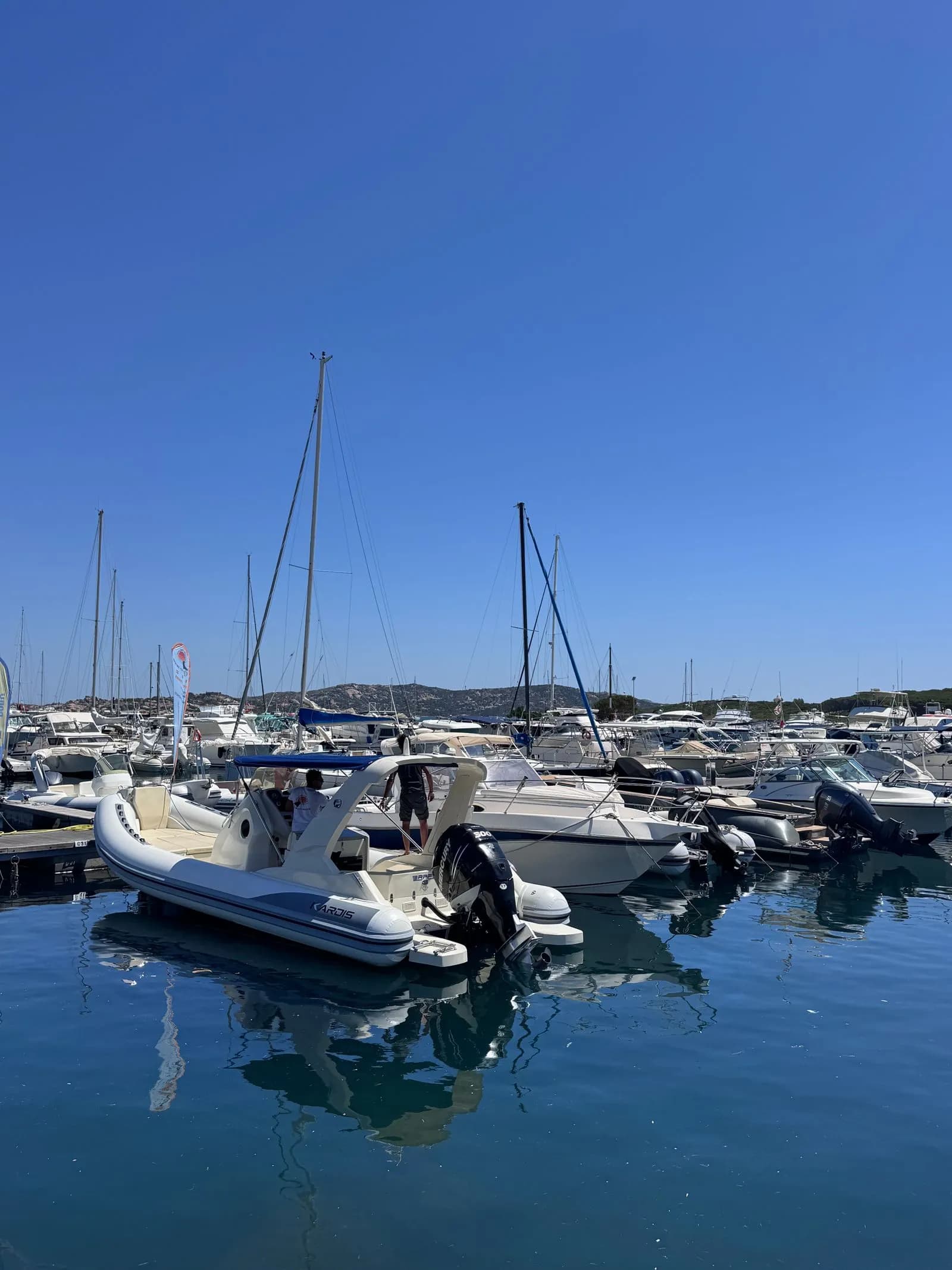 Gommoni e barche a motore ormeggiati in un porto turistico sotto un cielo azzurro