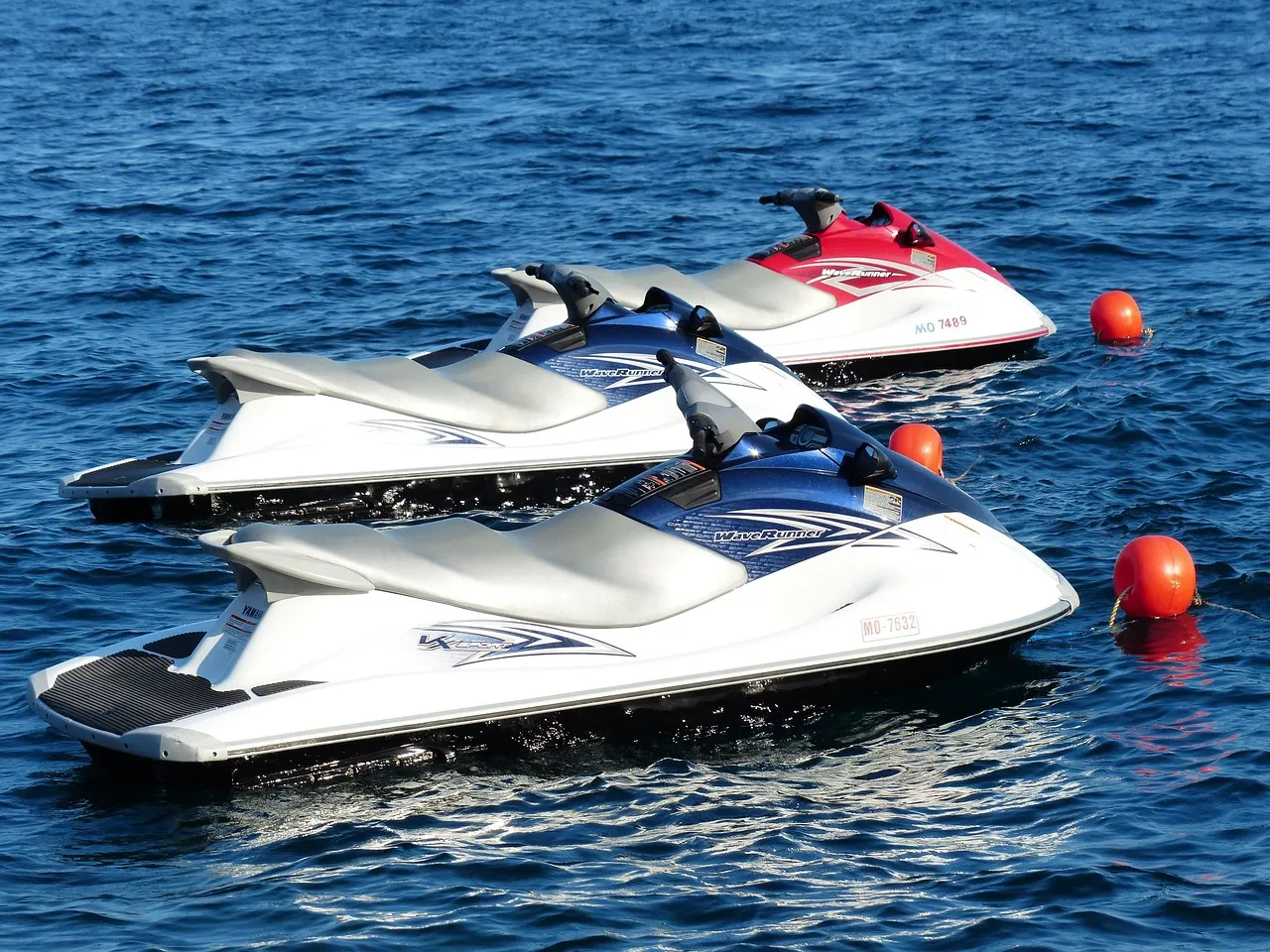 Tre moto d'acqua ormeggiate affiancate su acqua blu accanto a boe di segnalazione