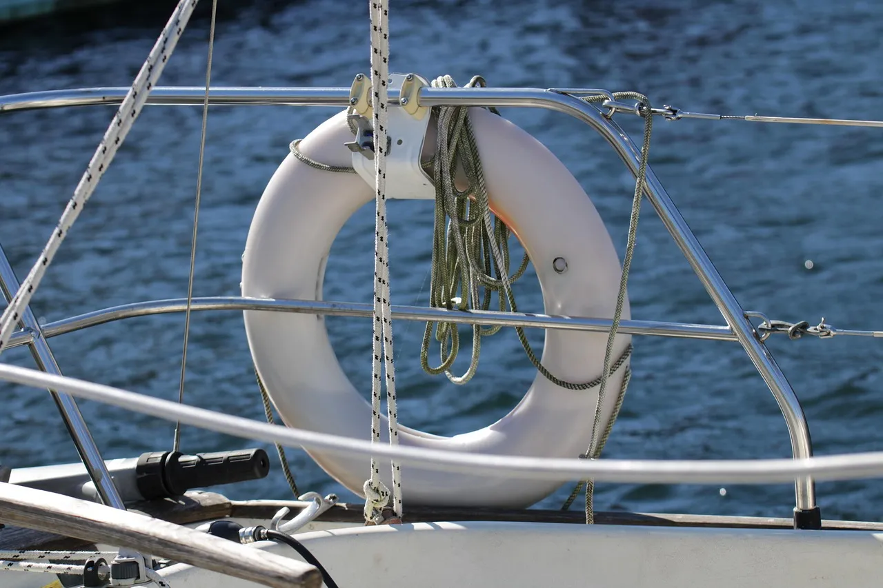 Salvagente anulare bianco con cima stivata, fissato al pulpito di una barca a vela sopra il mare aperto