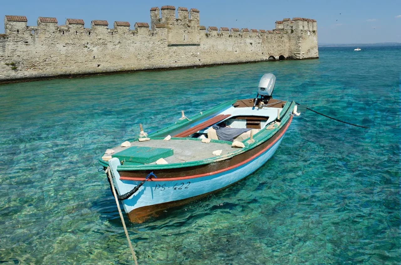 Barca in legno ormeggiata sull'acqua turchese davanti alle mura del castello Scaligero di Sirmione