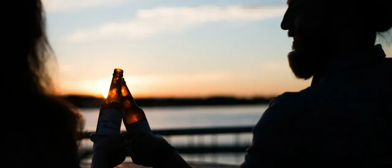 Coppia brinda con una birra a bordo di una barca al tramonto