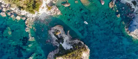 Veduta aerea di una cala rocciosa di Ponza con acqua turchese, scogli affioranti e una piccola barca all'ancora