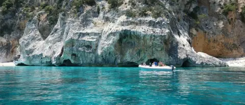 Una barca sotto le alte falesie bianche di una cala del Golfo di Orosei, a Cala Gonone