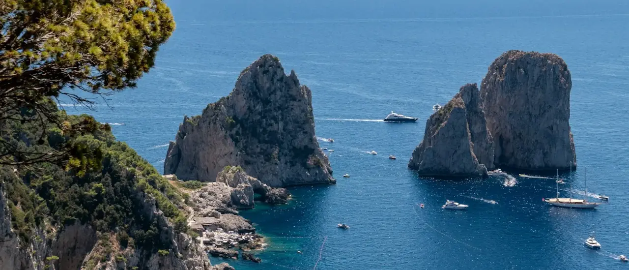 I Faraglioni di Capri visti dalla costa con alcune barche nel mare blu
