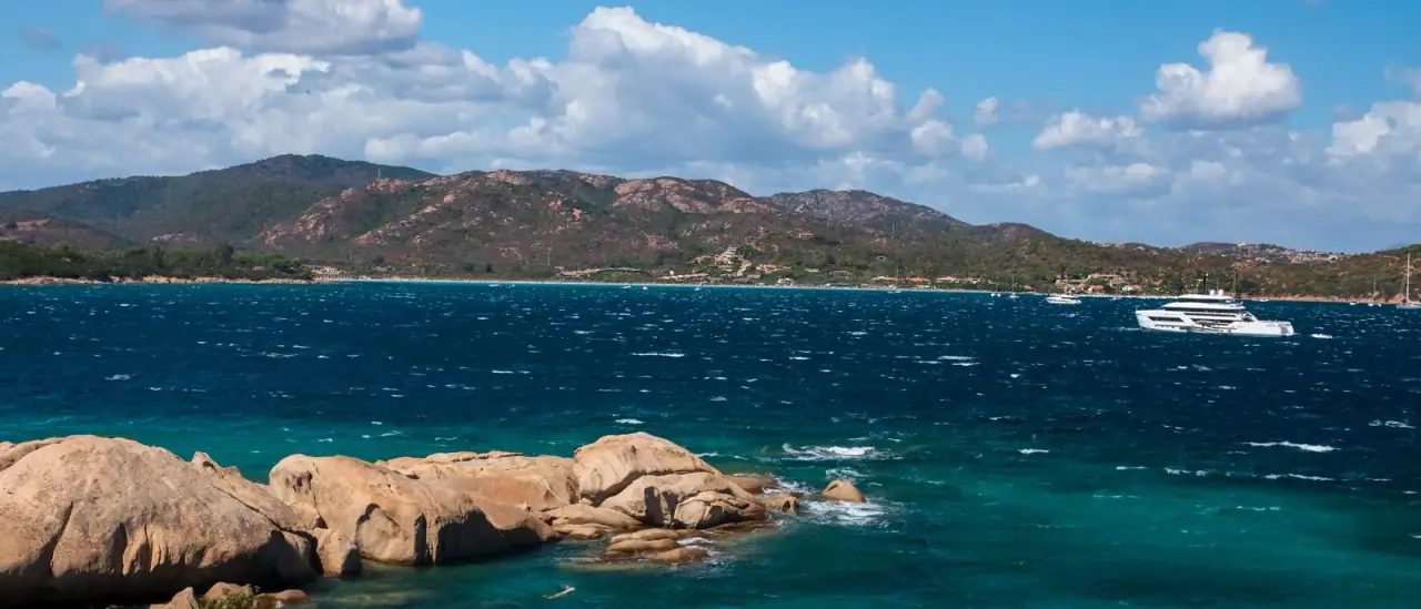 Costa rocciosa della Sardegna con acque turchesi e uno yacht all'ancora