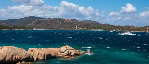 Costa rocciosa della Sardegna con acque turchesi e uno yacht all'ancora