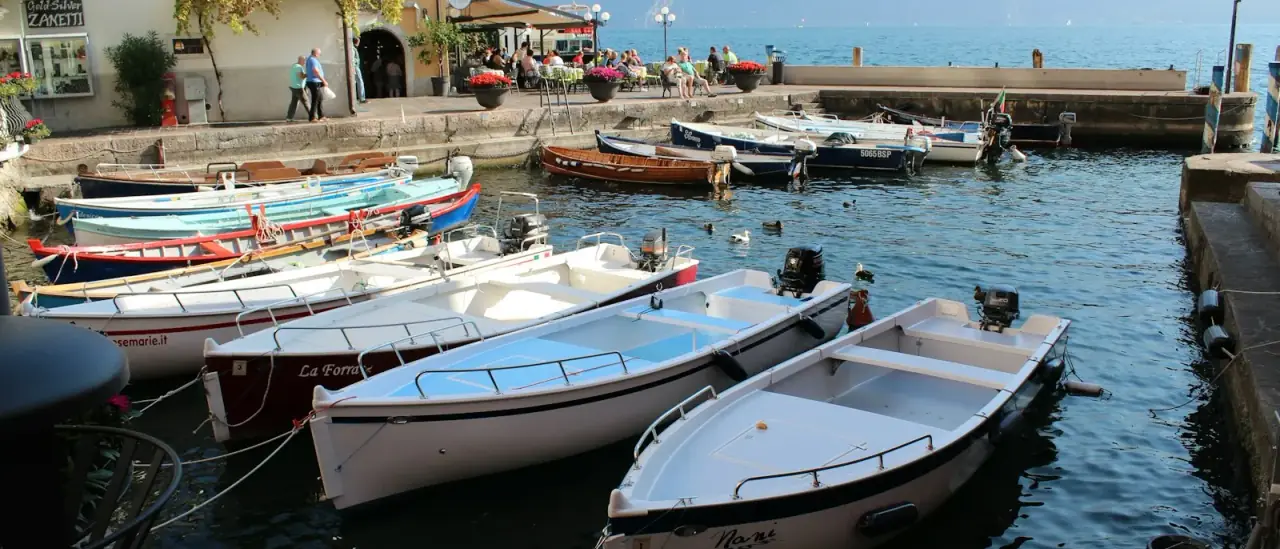 Una piccola barca a motore bianca e blu ormeggiata sul Lago di Garda a Limone