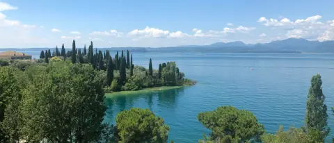 Veduta del Lago di Garda con un promontorio verde, barche e le montagne sullo sfondo