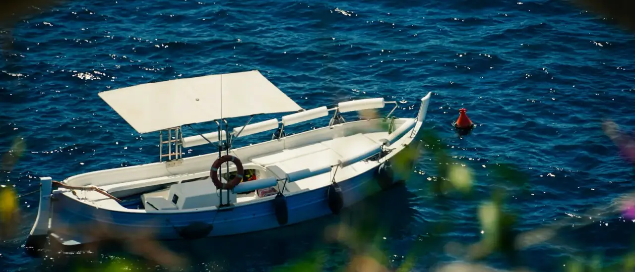 Piccola barca bianca ormeggiata su acqua blu lungo la costa italiana