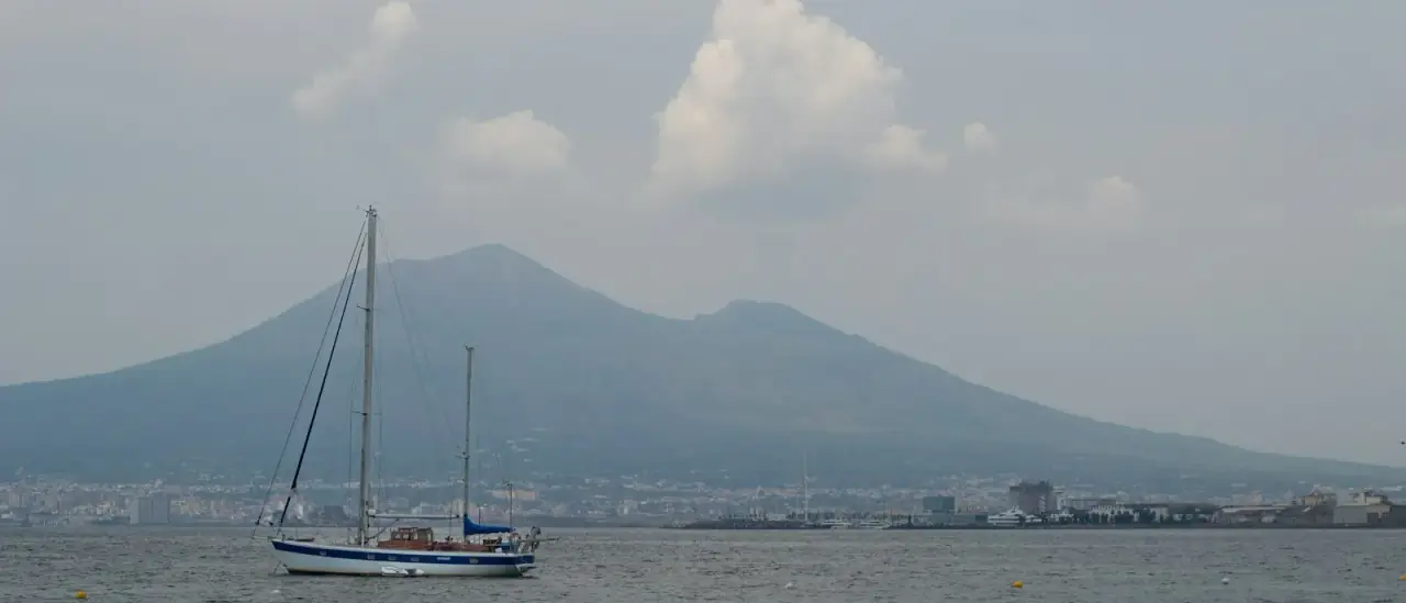 Una barca a vela naviga nel golfo di Napoli con il Vesuvio sullo sfondo