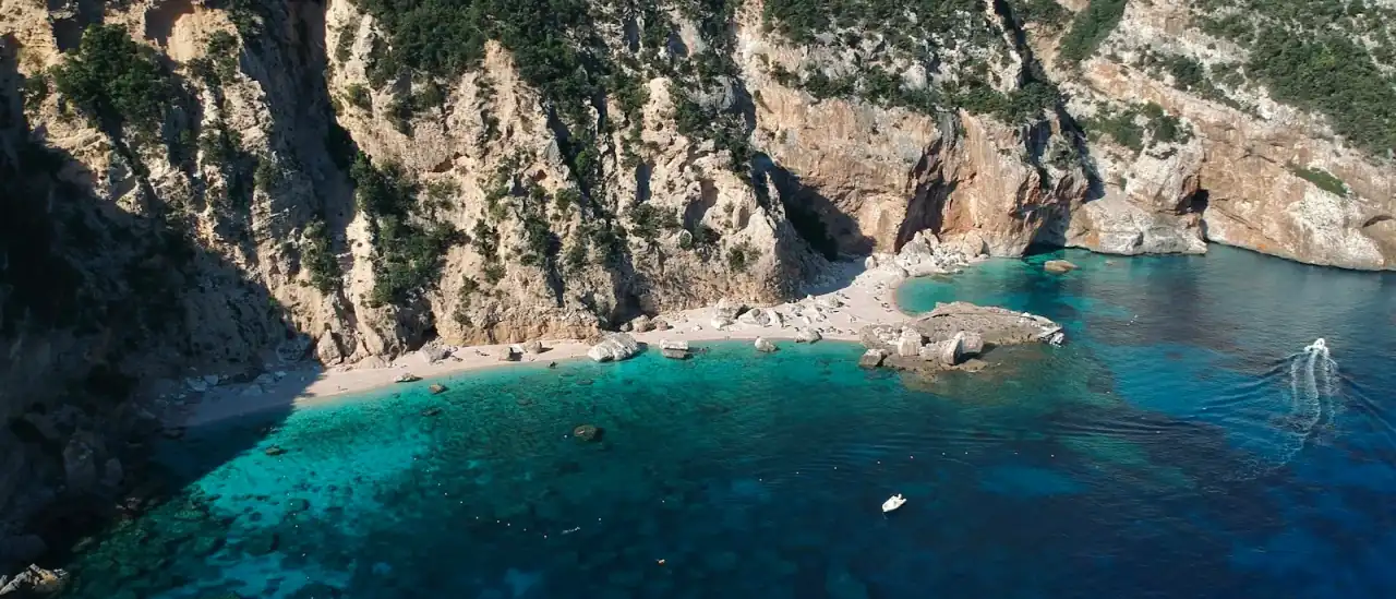 Una barca all'ancora nelle acque turchesi di una cala ai piedi di alte falesie