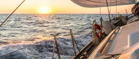 Barca a vela in navigazione al tramonto, vista dal ponte verso le vele
