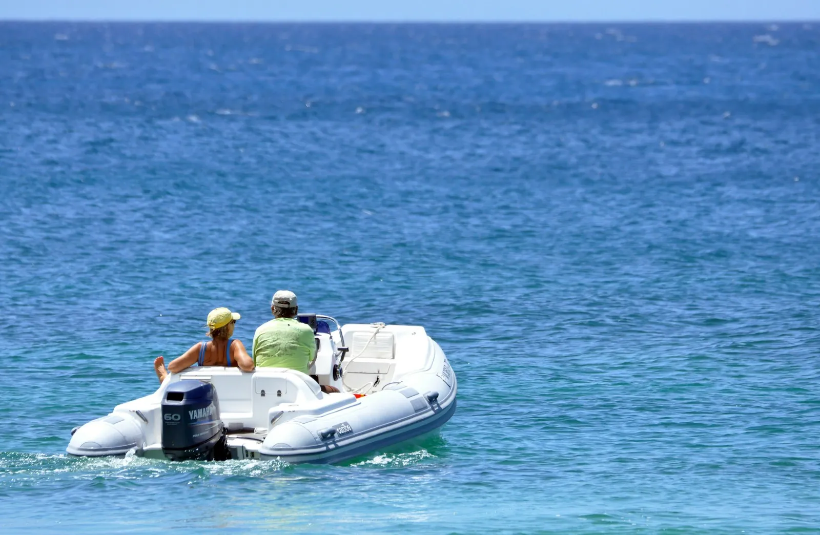 Coppia a bordo di un gommone in navigazione su mare azzurro lungo la costa
