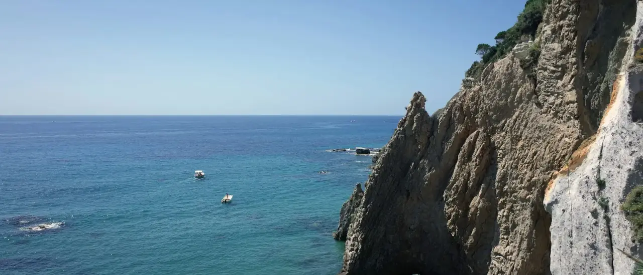 Falesia calcarea e arco naturale sulla costa di Ponza con piccole barche sul mare turchese
