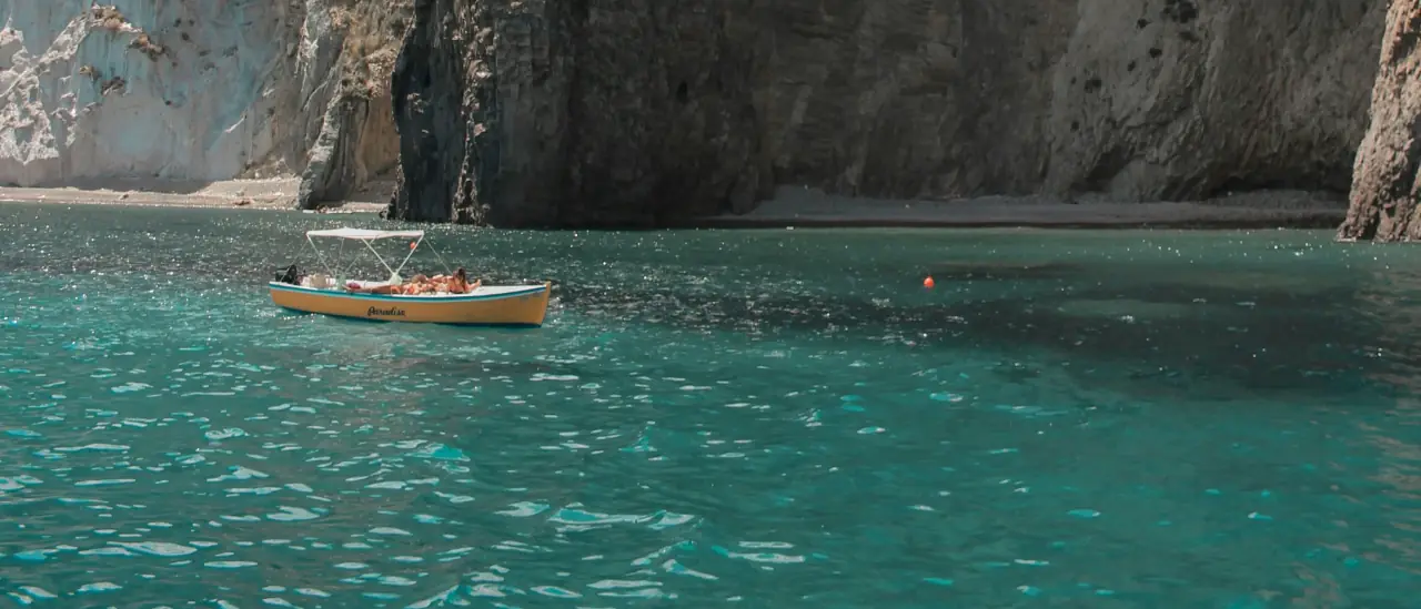 Gommone con turisti ancorato davanti alle falesie di Ponza in acqua turchese