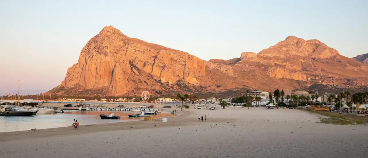 La spiaggia di San Vito Lo Capo con barche tirate a riva e il Monte Monaco sullo sfondo al tramonto