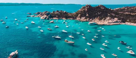 Numerose barche a vela e a motore all'ancora nelle acque turchesi di una cala della Sardegna