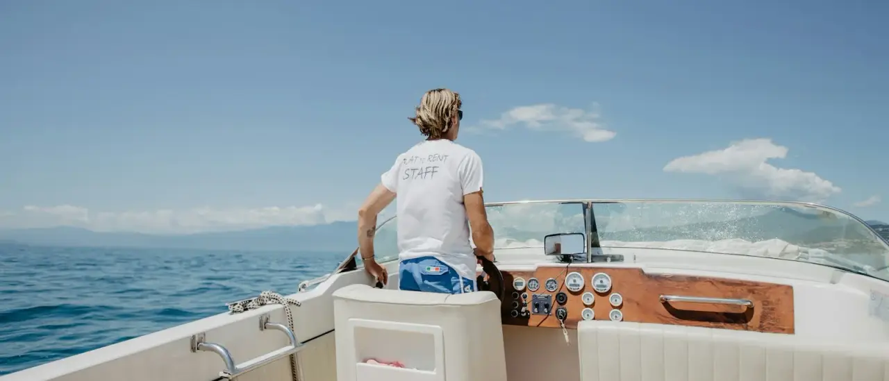 Membro dell'equipaggio in maglietta staff alla guida di una barca a motore in acque italiane